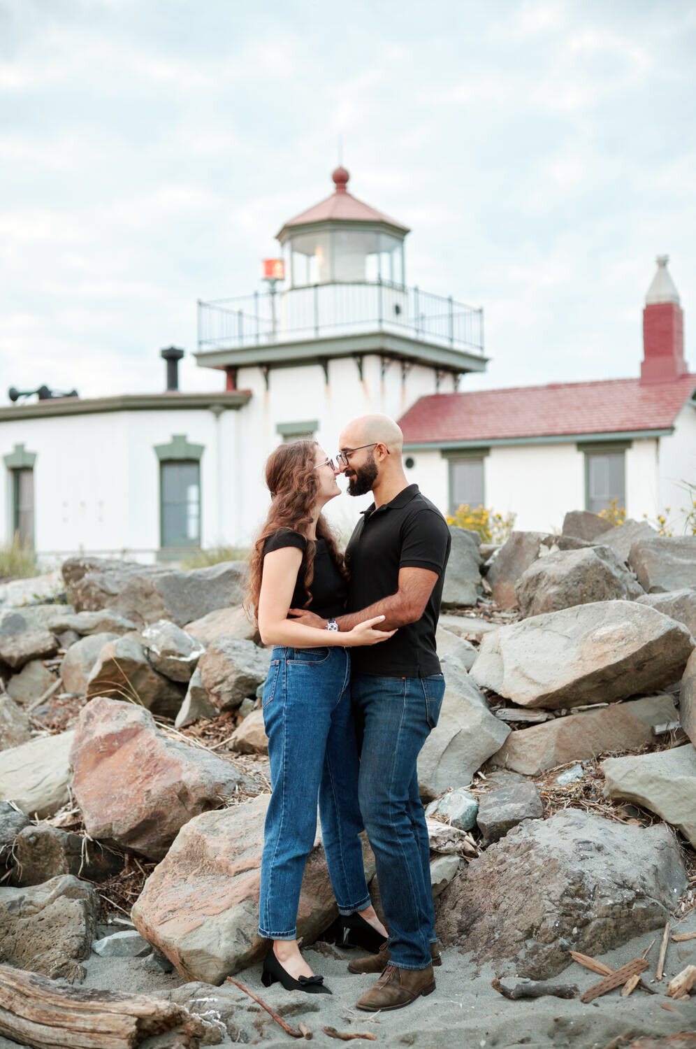 Couple stands in front of a lighthouse for an engagement portrait