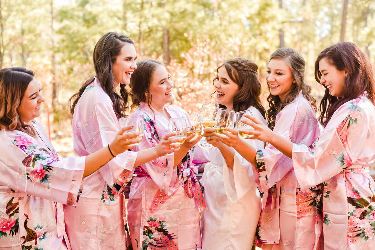 Bride with bridesmaids cheers with drinks in pink floral robes Flagstaff Mormon Lake Wedding
