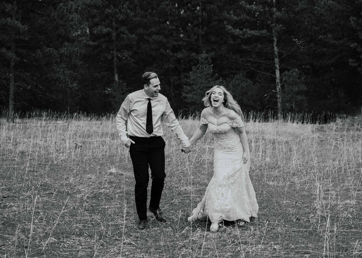 Maddie Rae Photography black and white of bride and groom walking towards the camera holding hands. he is looking at her and she is laughing looking at the camera