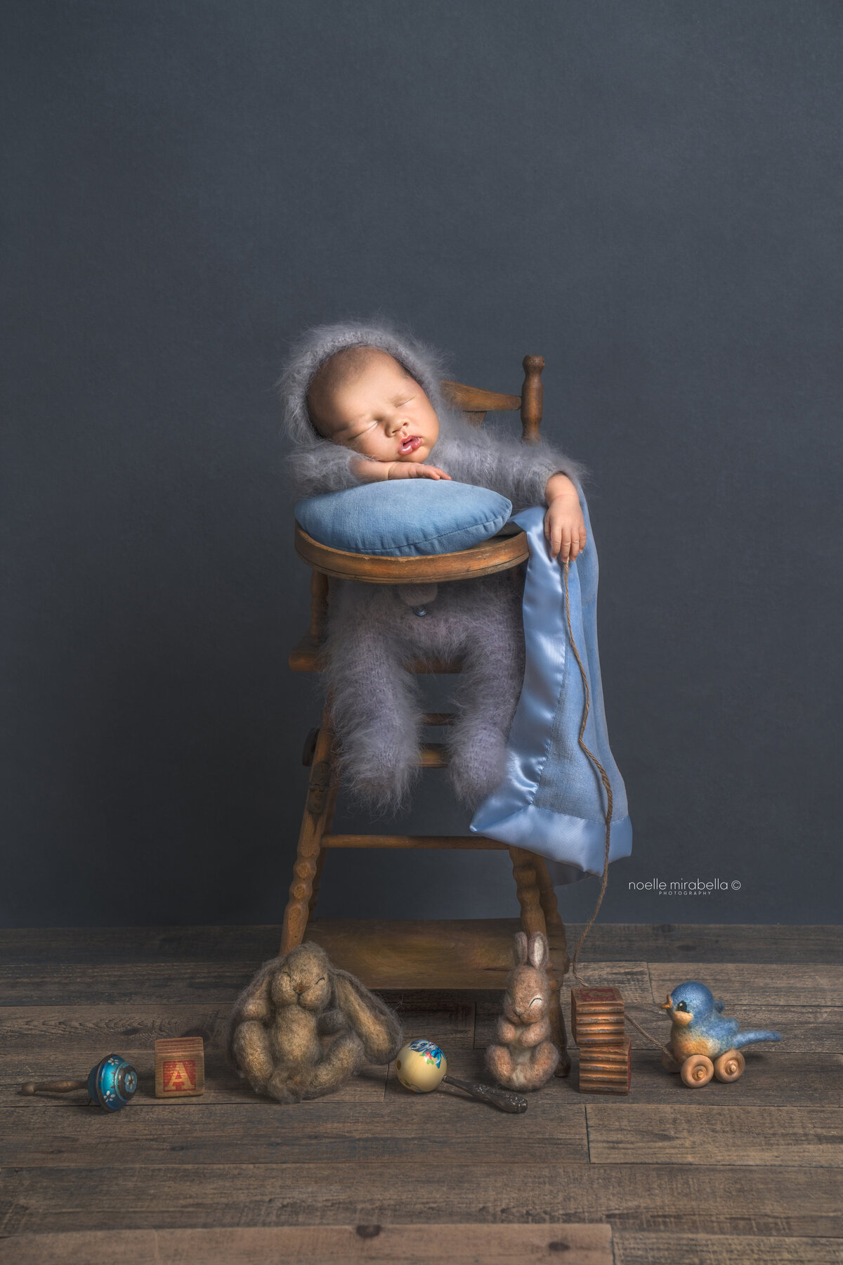 Newborn baby sleeping in vintage wooden high chair. Pale blue pastel tones. Vintage baby toys.