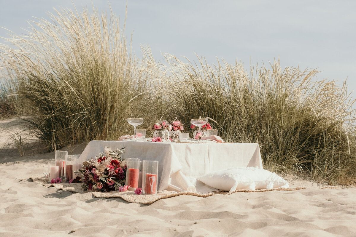 Am Strand ist ein niedriger Tisch mit rosa Rosen, Kerzen und Champagnerkelchen geschmückt.