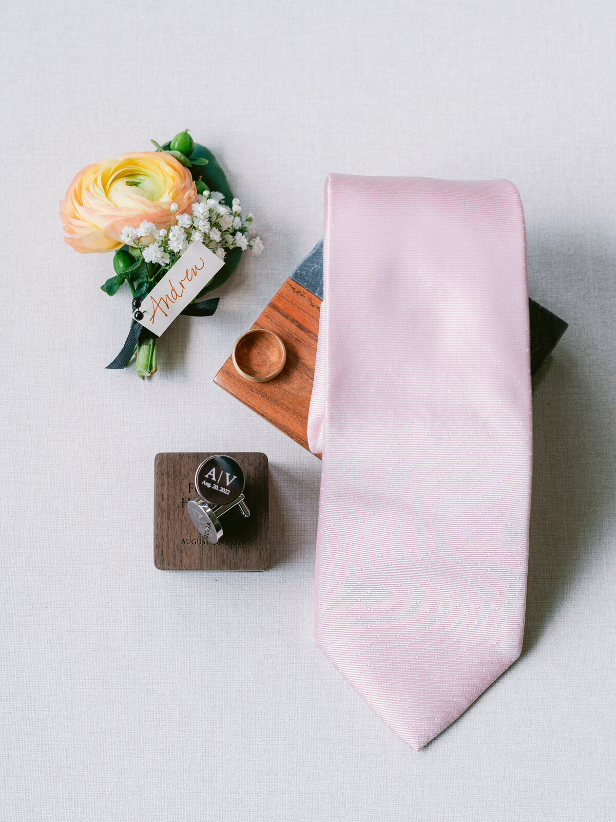 Flatlay of wedding details including tie, rings and florals