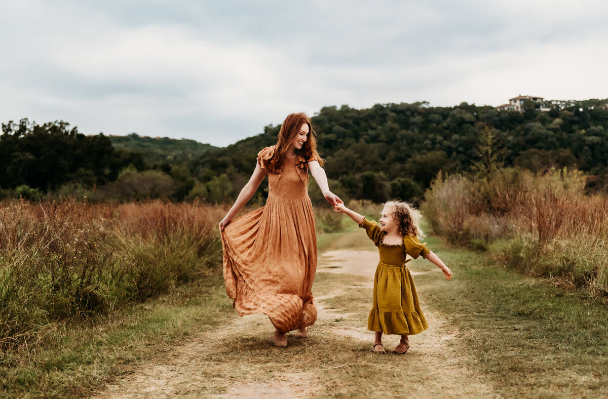 Mom  holding daughter's hand and twirling with her in the grass.