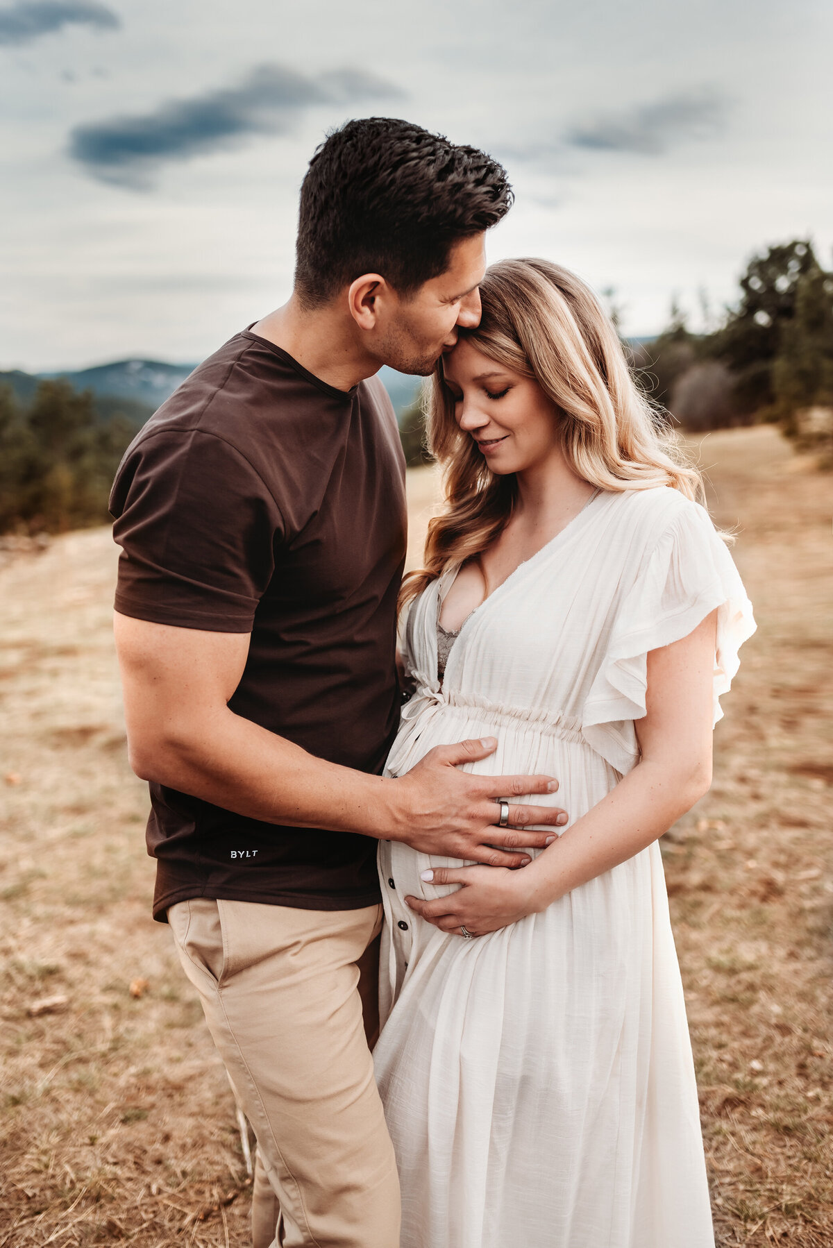 husband kissing maternity wife standing in a field