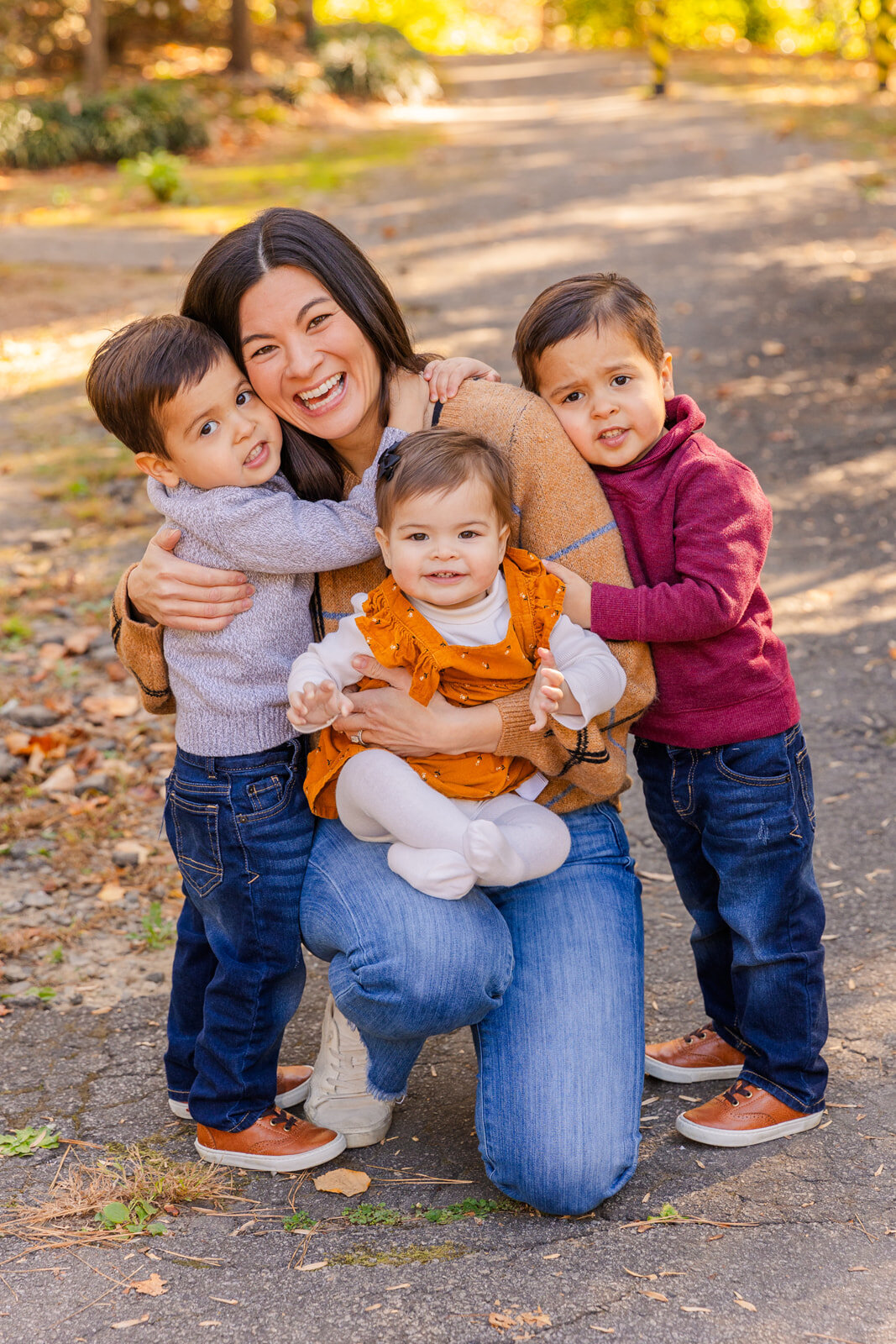 mommy kneeling on a park path laughing and hugging her 3 toddlers during photoshoot with Laure Photography
