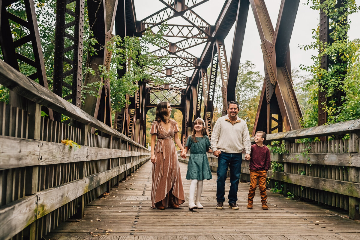 A family of four, walking on a bridge in Collinsville, CT, holding hands.
