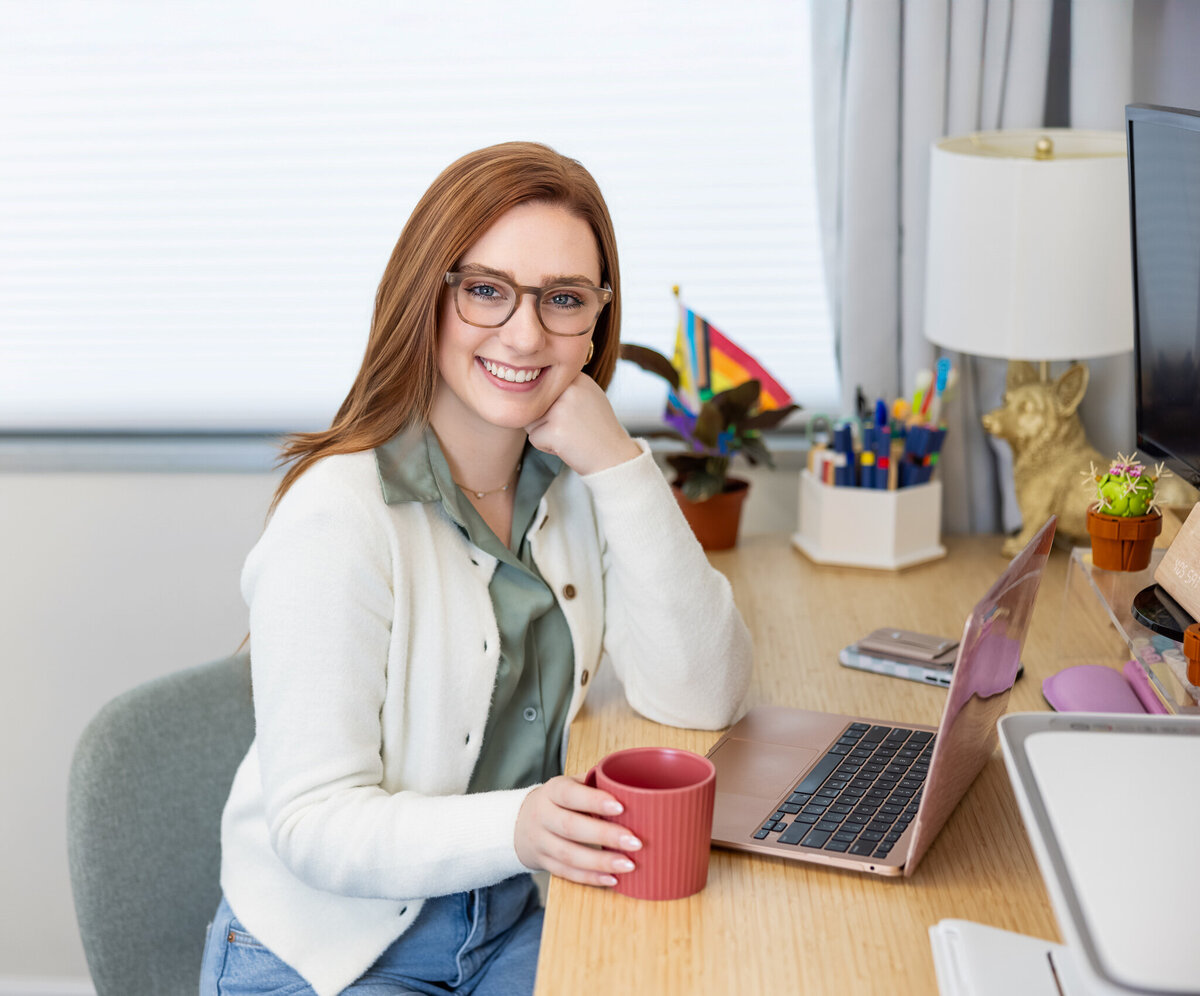 Female-therapist-sits-at-desk-with-laptop-smiling-for-her-brand-session-with-photographer-ingrid-berrios