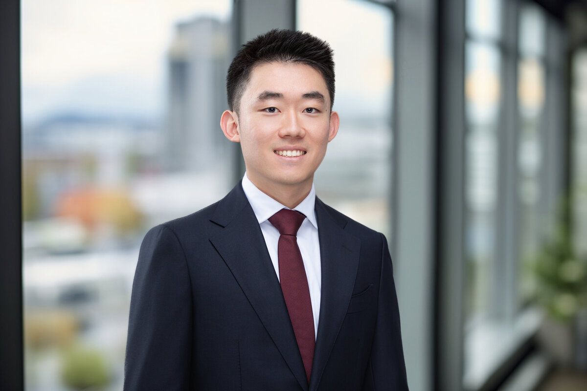 Professional headshot of an Asian man in a business suit with a red tie, taken at a Cincinnati studio. The background features a modern office setting with large windows, highlighting the cityscape. This high-quality image is perfect for personal branding and corporate profiles in Cincinnati. Enhance your professional presence with expert headshot photography in Cincinnati.