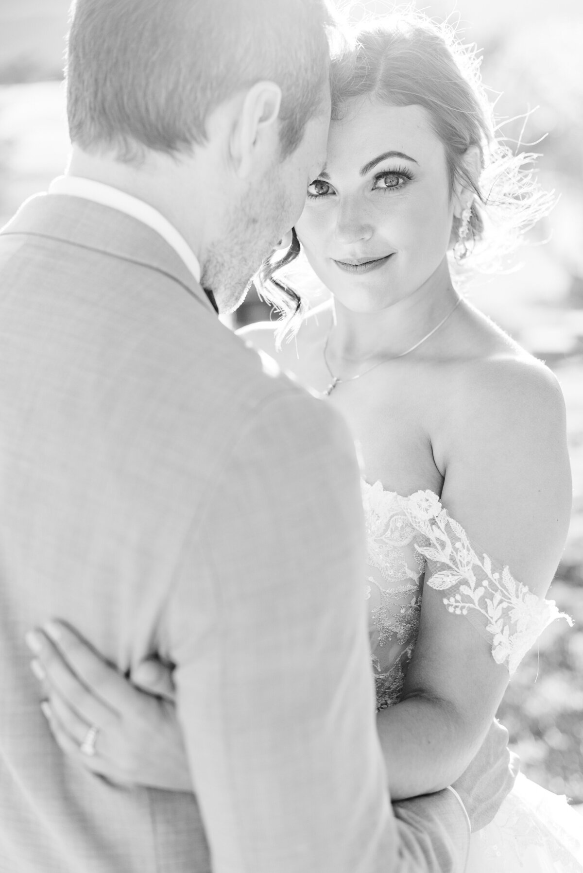 Black and white photograph of a bride looking over her groom's shoulder at the camera.
