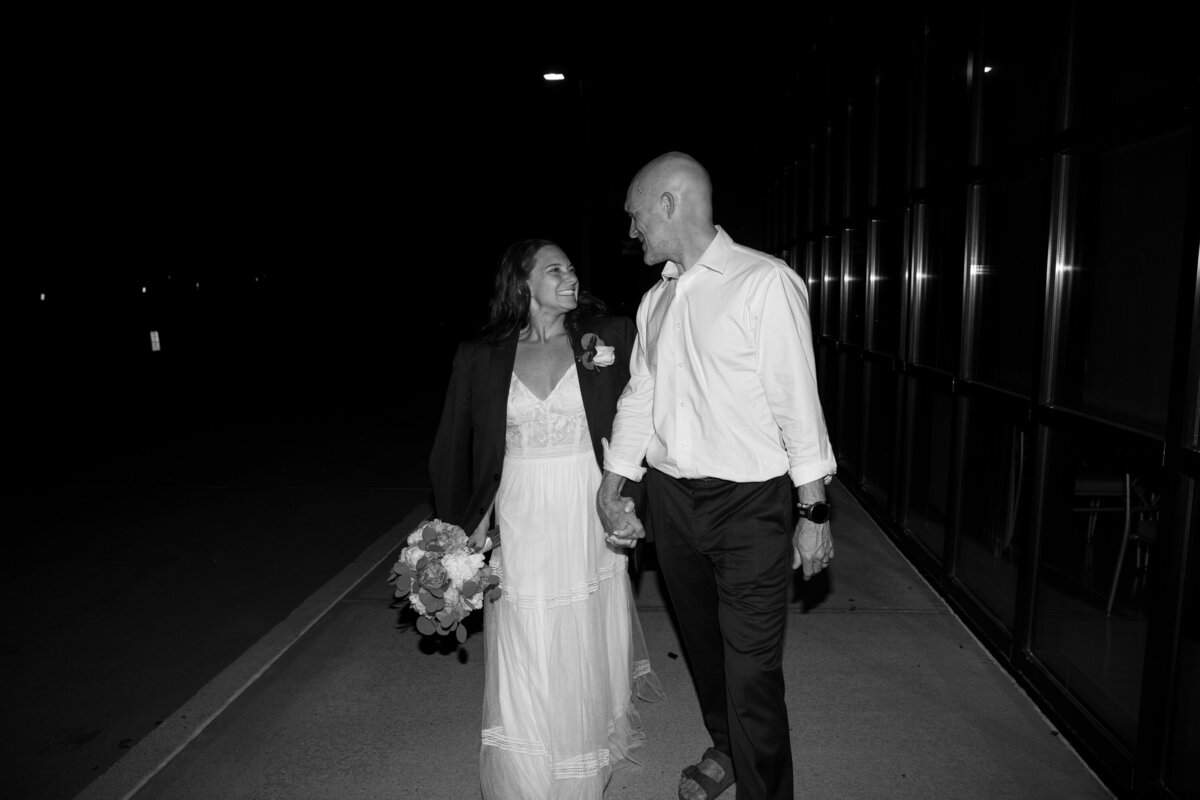 black and white photo of a bride walking with groom wearing his jacket and carrying flowers Hotel Nyack direct flash wedding photography Milestone Images