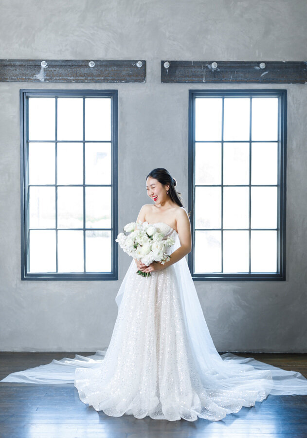 Bride smiling in a wedding dress with a white bouquet of flowers.