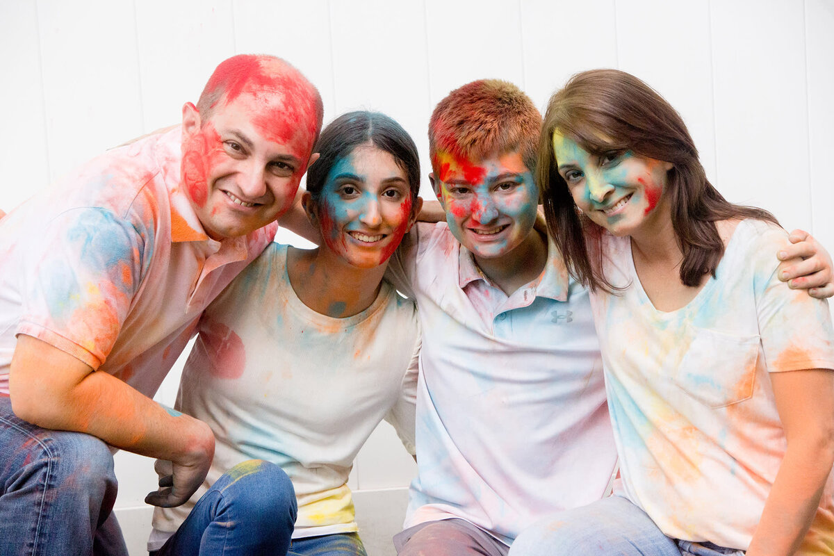 A family of four covered in colored holi powder poses for a photo New City family portrait photographer Milestone Images