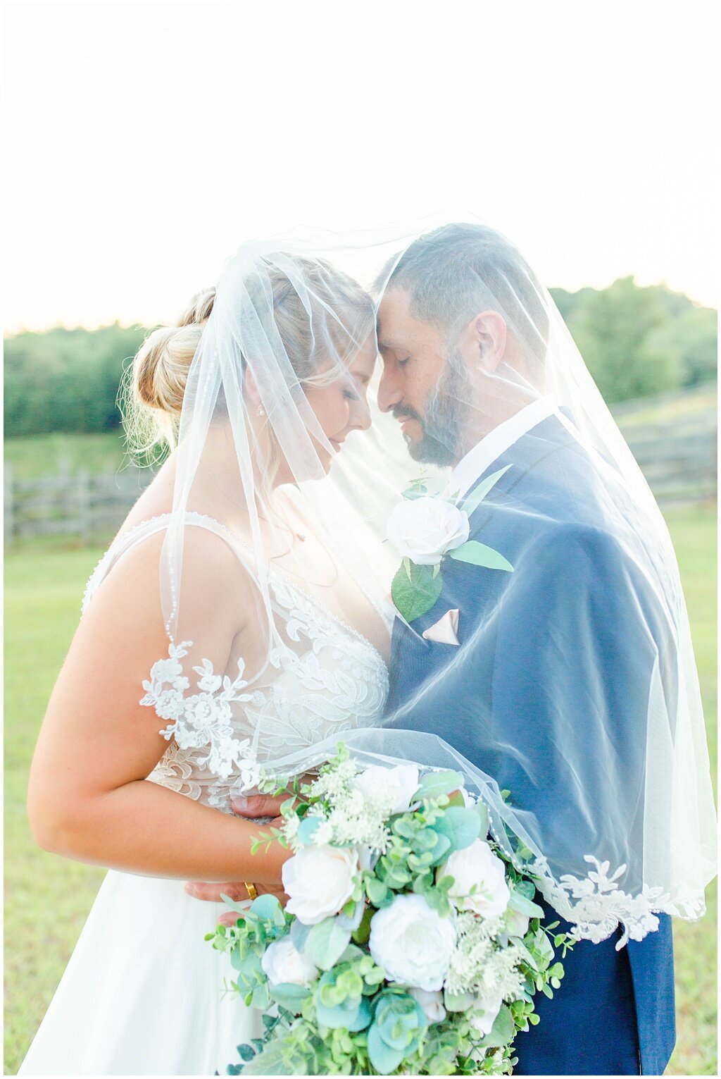 bride and groom standing with veil over head forehead to forehead