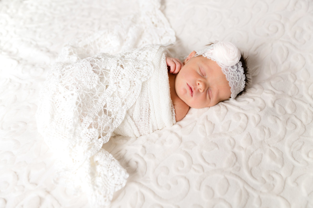 newborn baby swaddled in white blanket laying on a white blanket