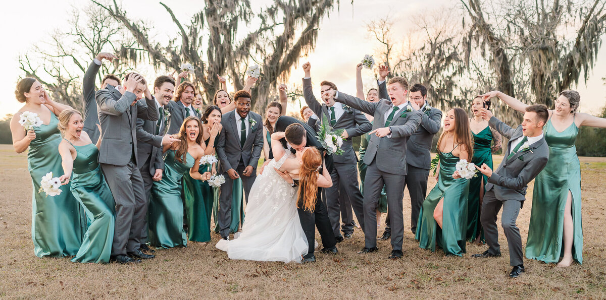 A bride and groom kissing next to their wedding party at sunset while enjoying their Raleigh wedding photos