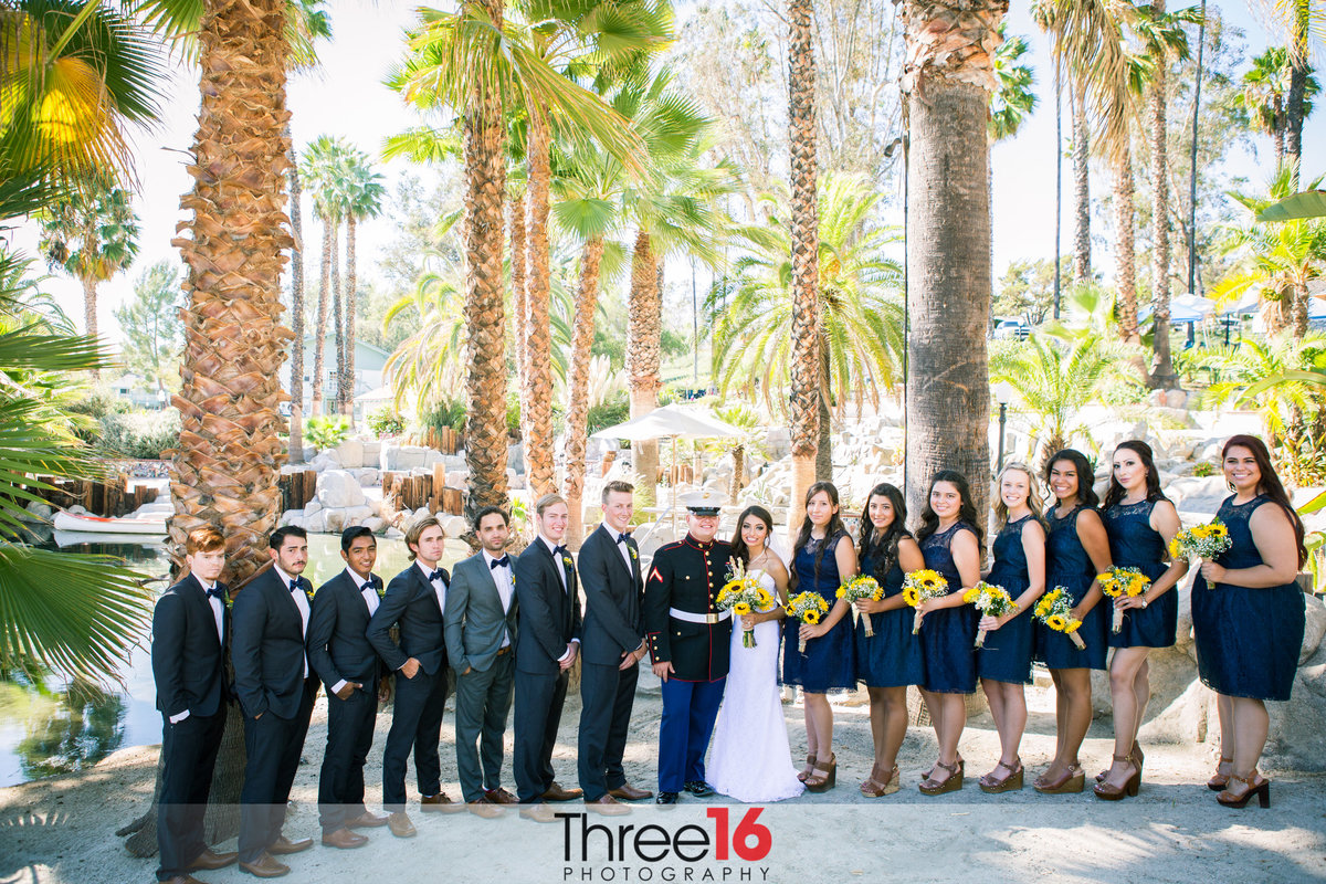 Bride and Groom pose with their wedding party in front of the palm trees at Calvary Chapel in Murrieta