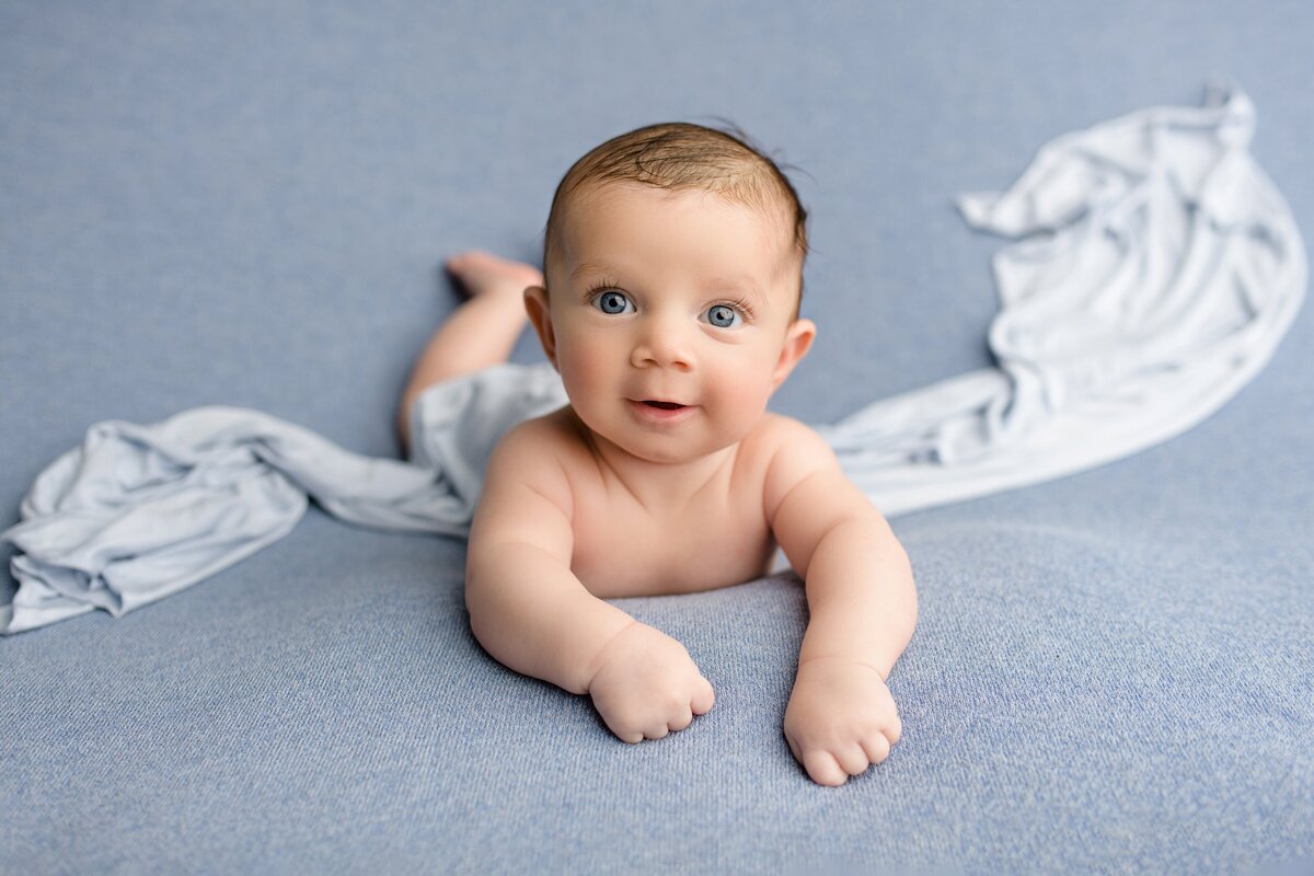 4 month old baby boy laying on his belly on a blue studio backgroud