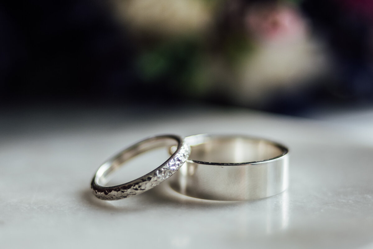 Two rings sat slightly on top of each other with flowers in the background taken by London Wedding Photographer Liberty Pearl