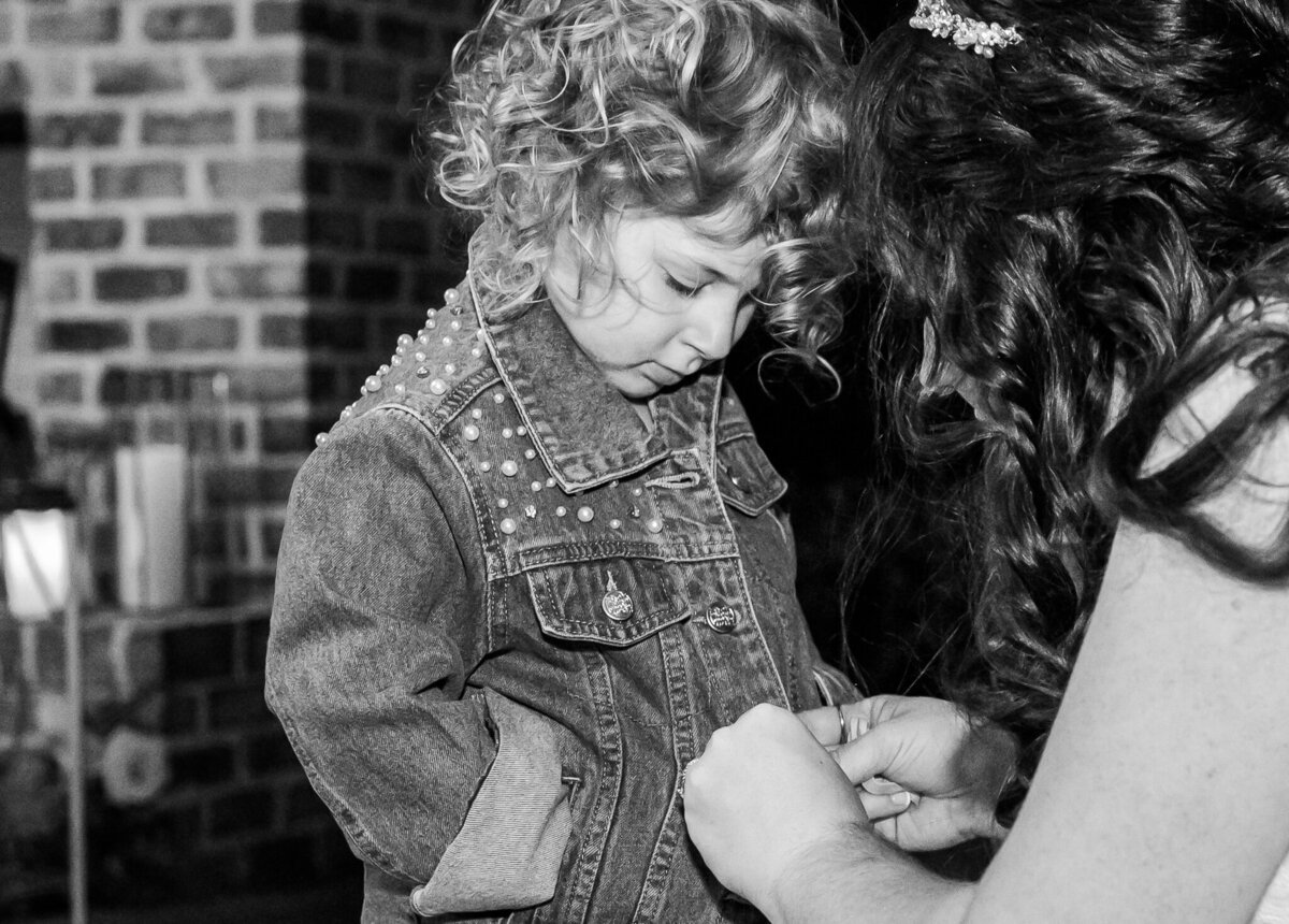 A bride on her wedding day zipping the coat of her daughter during the wedding reception by JoLynn Photography, a Raleigh wedding photographer