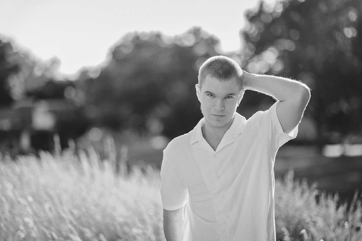 Black and white picture of a senior guy in a field with his hand behind his head