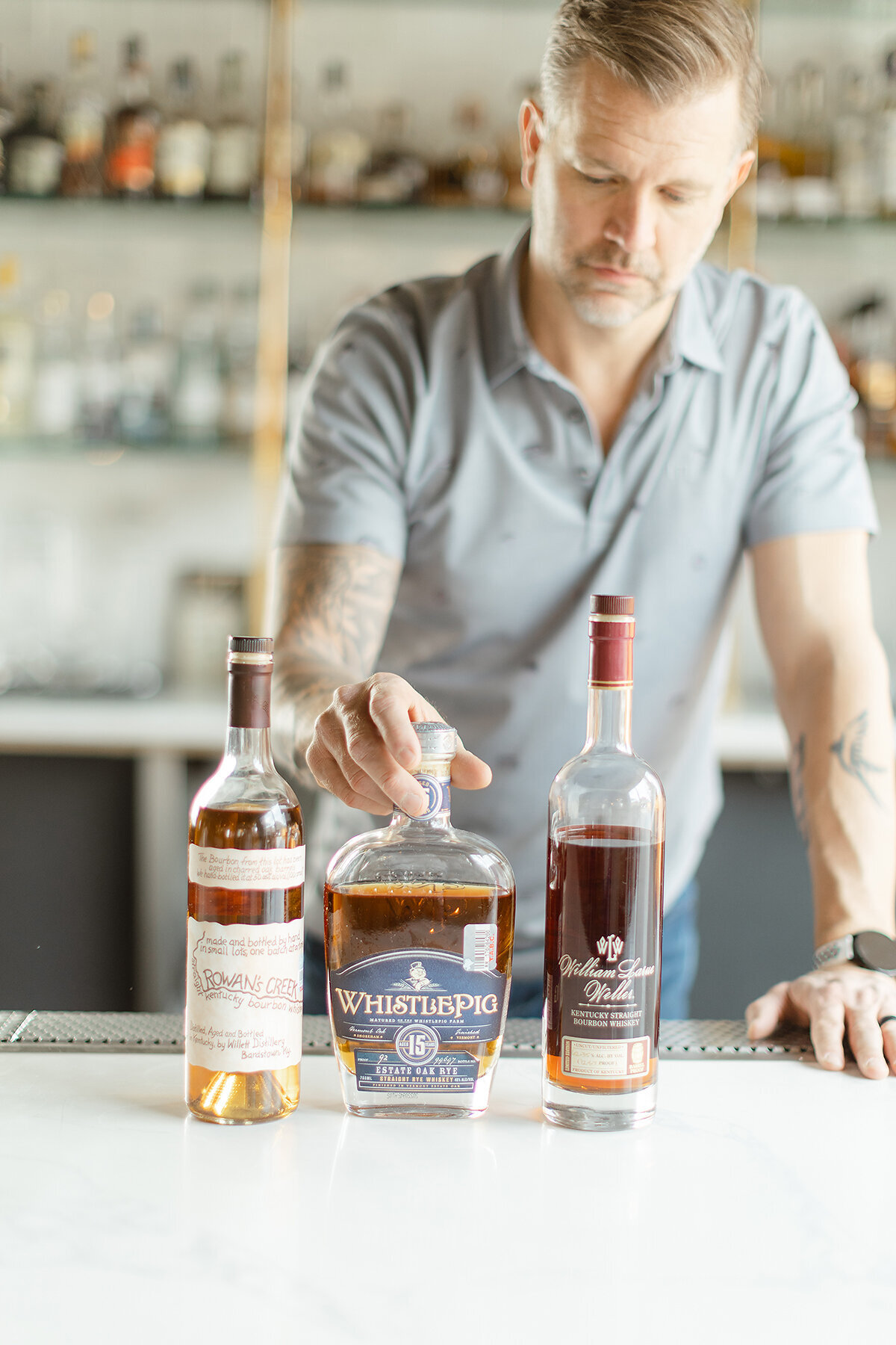 Professional headshot of a Dallas/Fort Worth business owner at his new restaurant Sip and Savor as he stands at the bar holding a bottle of alcohol.