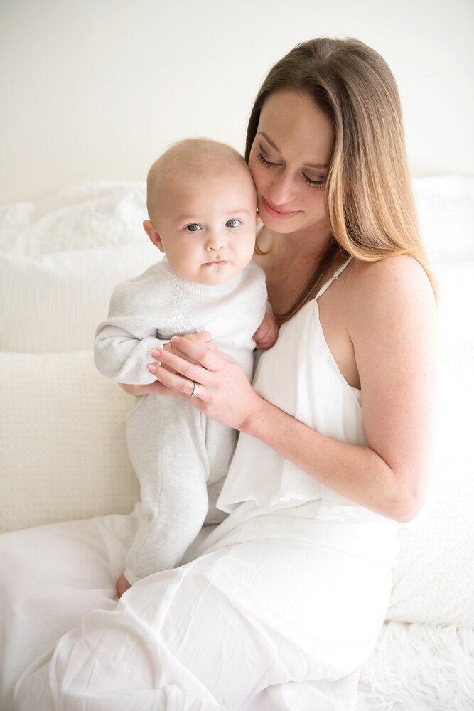 Family session of little boy and his mother sitting on a bed