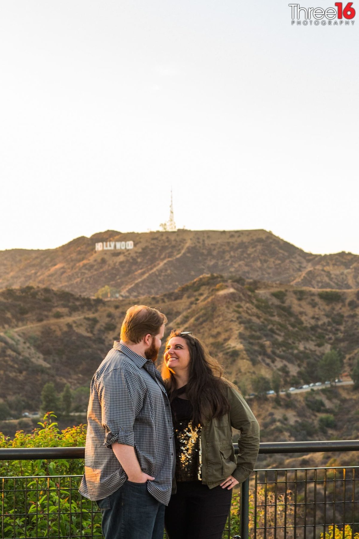 Engaged couple look into each other's eyes and smile while overlooking the hills and ravine outside at the Griffith Observatory