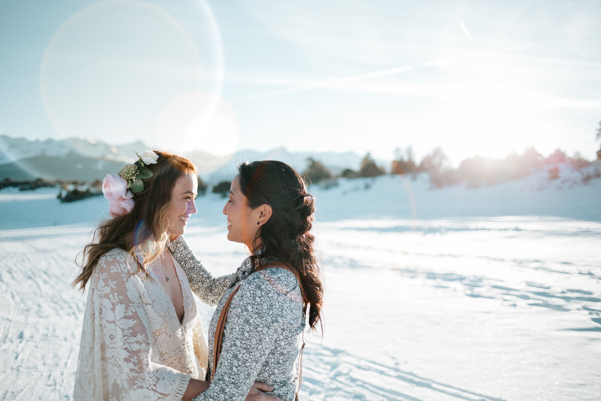 Snowy elopement with two brides  looking at each other in the the sunshine