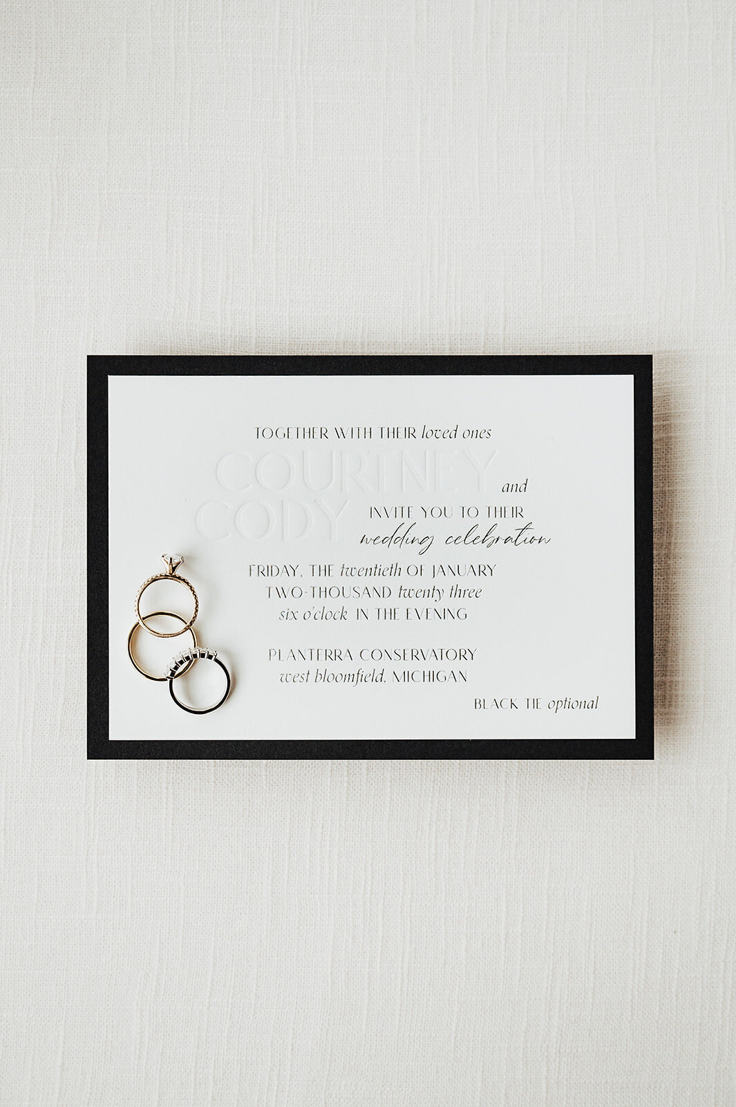 A black and white debossed custom wedding invitation with wedding rings on it against a white background from alyssa amez design's custom wedding stationery and signage