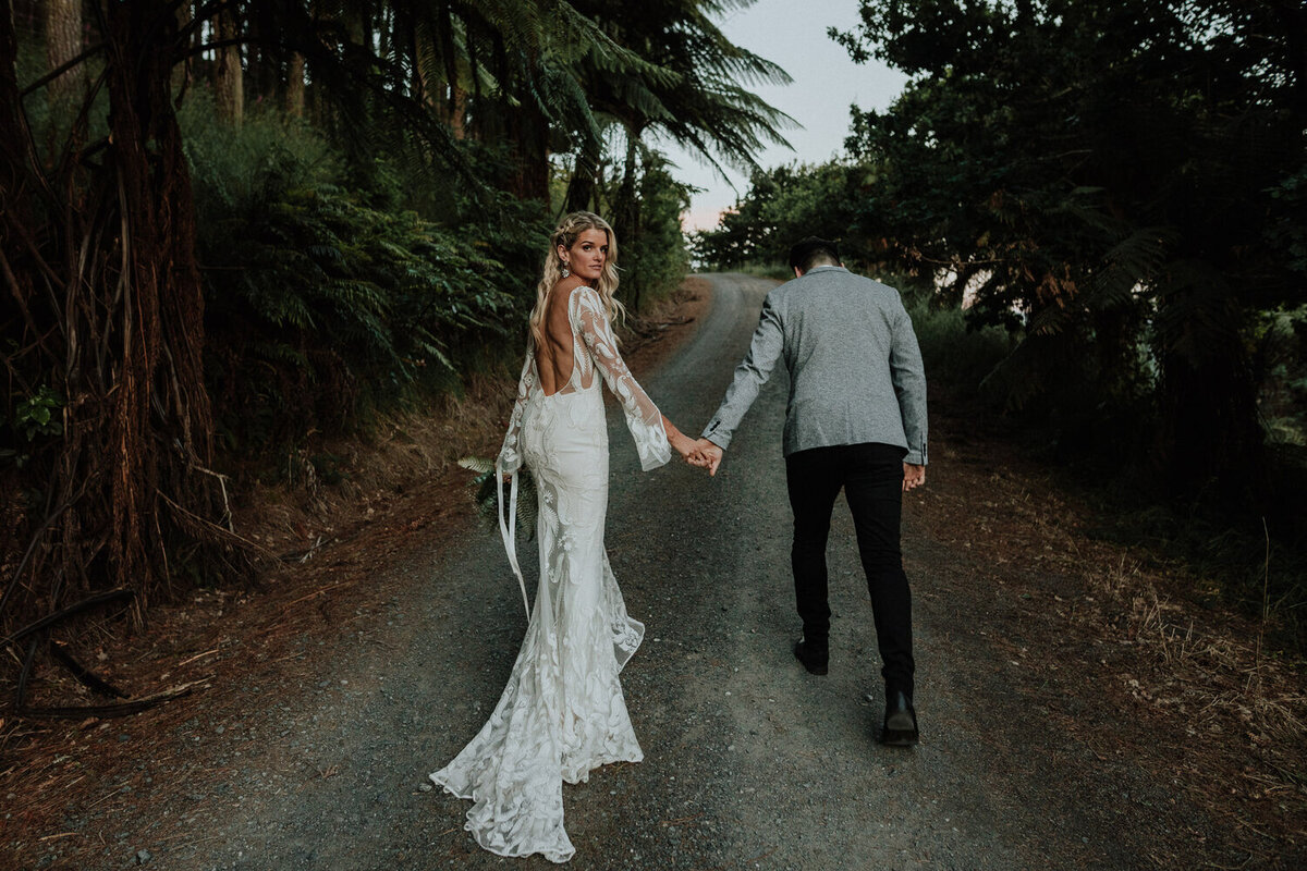 Bride and groom outside holding hands walking down a forest road