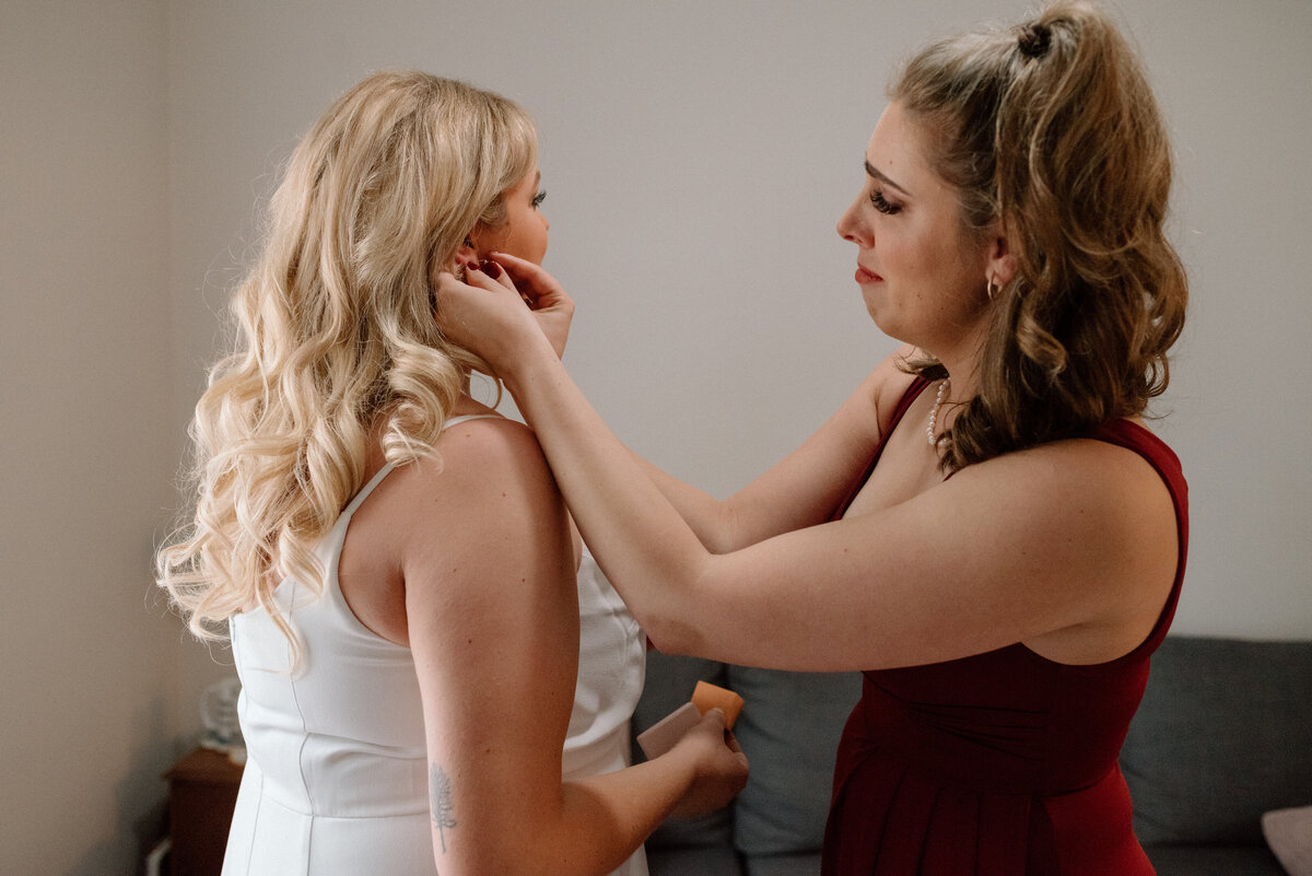 sister of the bride holds back tears as she helps her sister with her earrings