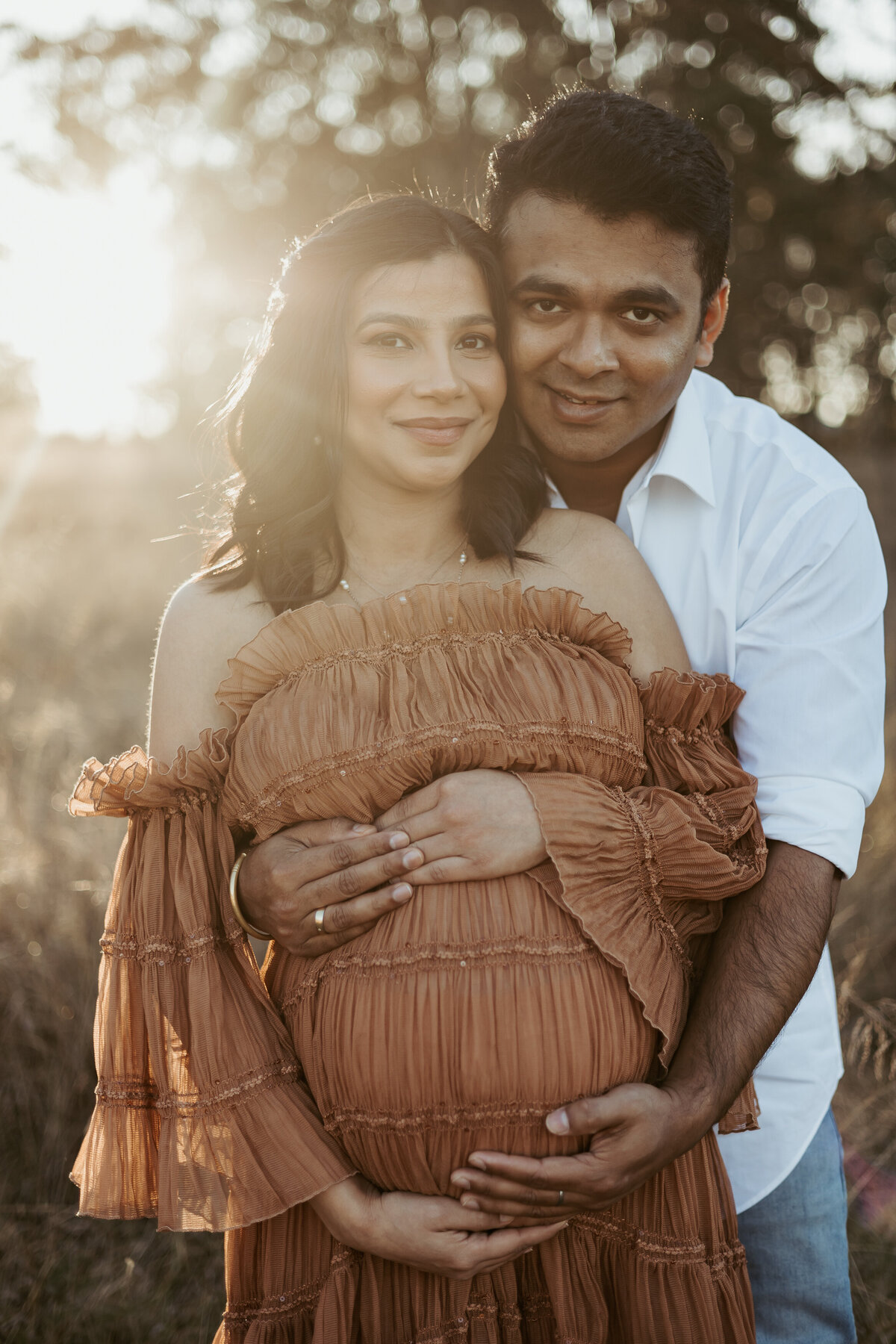 Parents cradling mama's pregnant bump while gazing straight at the camera