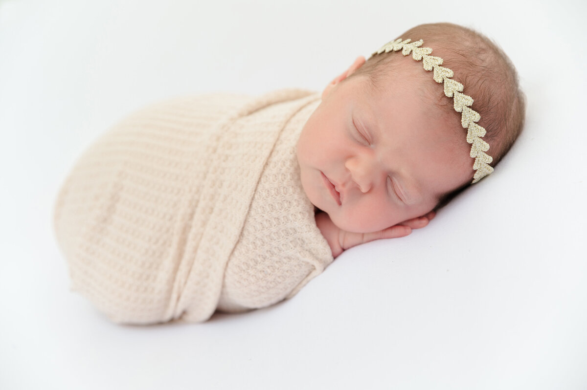 Newborn  baby laying on tummy swaddled in a pastel pink swaddle in a studio.