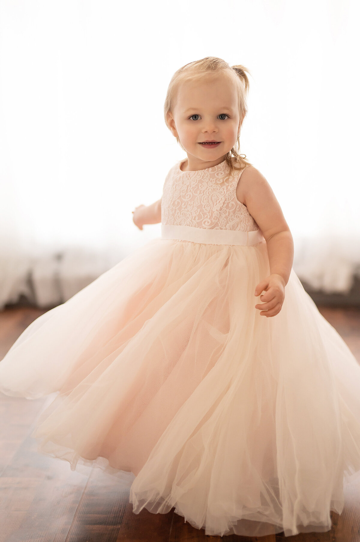 A toddler girl twirls around our Waukesha photos studio in a light pink gown.