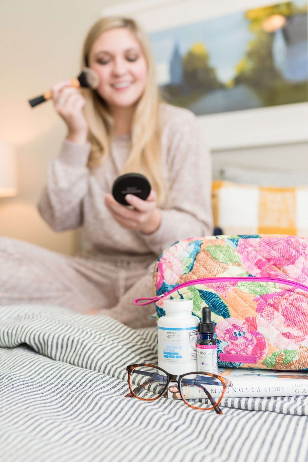 Product photo of Humarian probiotics with a make up bag and glasses and a woman blurry in the background apply makeup