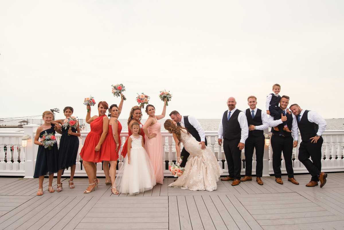 photo of full bridal party with bride and groom kissing in the middle for wedding at Lombardi's on the Bay