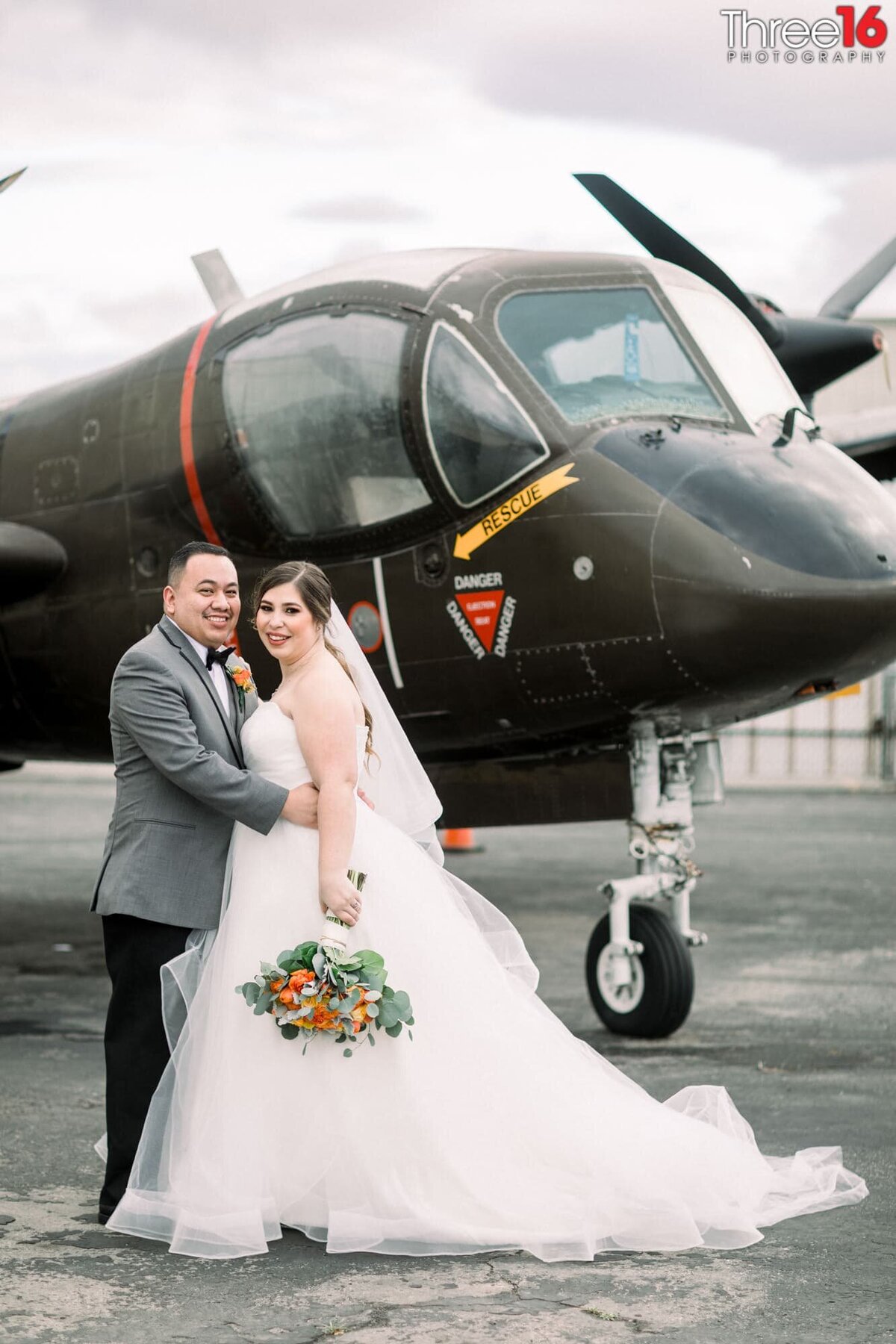 Bride and Groom pose for photos in front of a plane as the Groom holds his Bride
