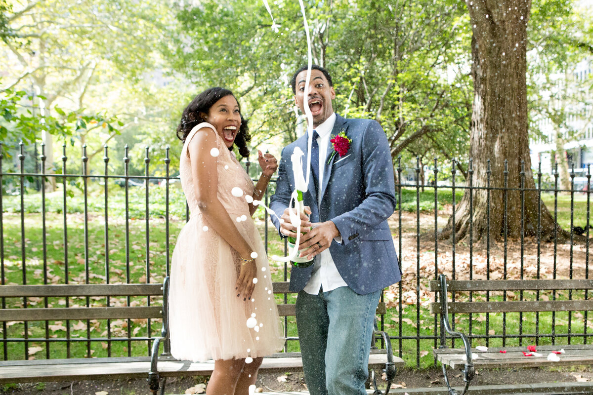 A Black woman in a pink dress and her fiance in a blue suit spray champagne Gramercy Park engagement session New York wedding photographer