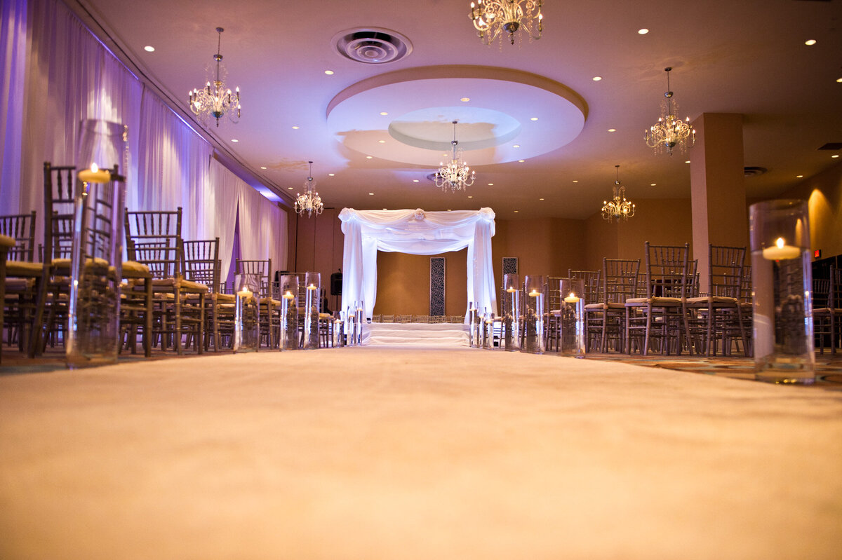 Indoor wedding ceremony site with white draping and florals