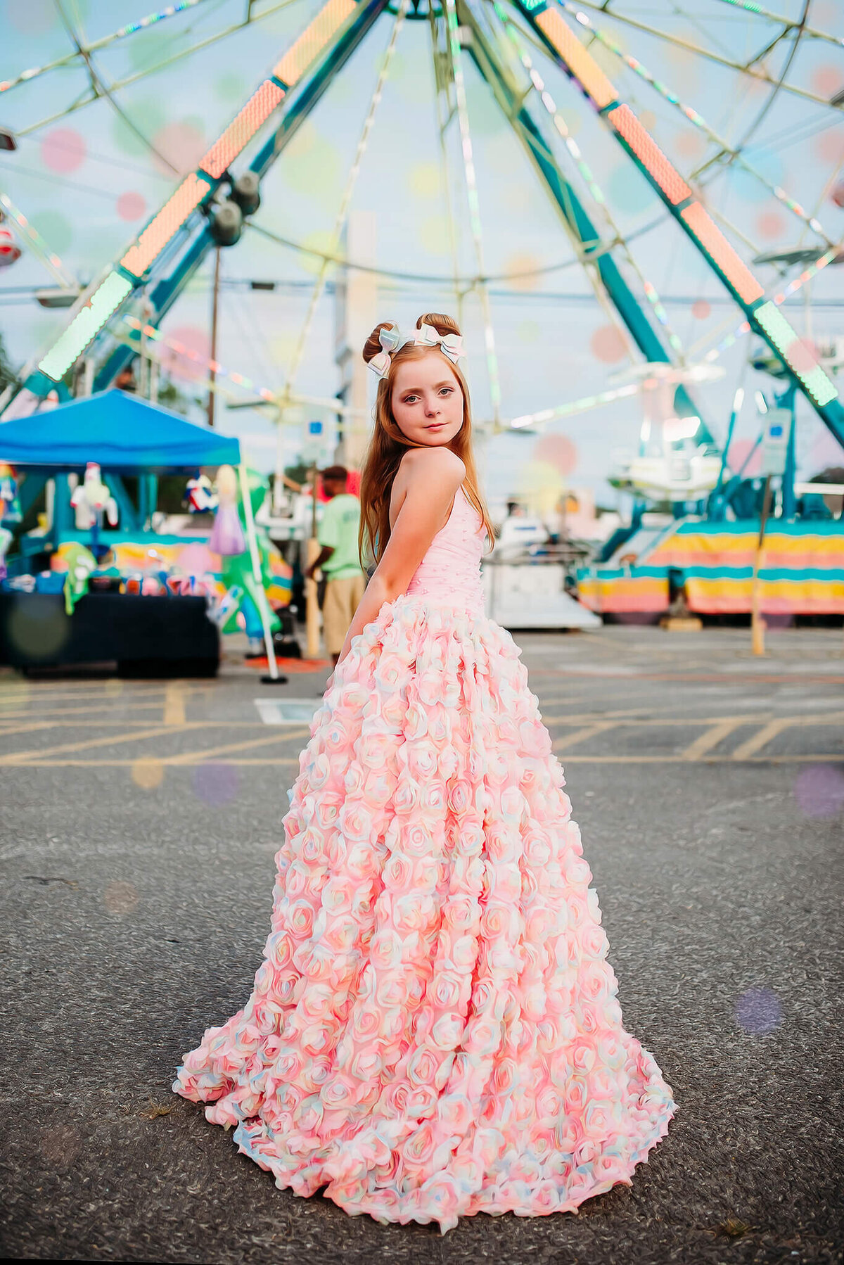 red haired girl in a pink rainbow dress standing in front of a ferris wheel at a carnival near Annapolis Maryland
