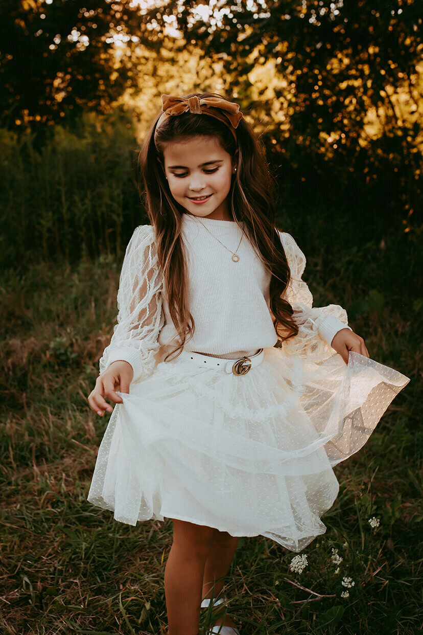 a six year old girl holding her dress as she dances through a field in rochester, ny
