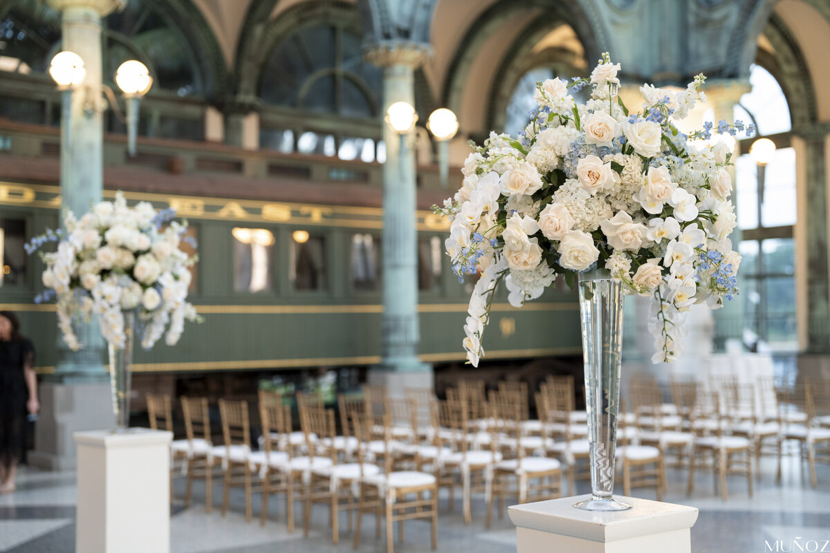 An elegant indoor wedding setup with tall white floral arrangements and rows of chairs, showcasing Socially Significant Events’ luxury event planning style.