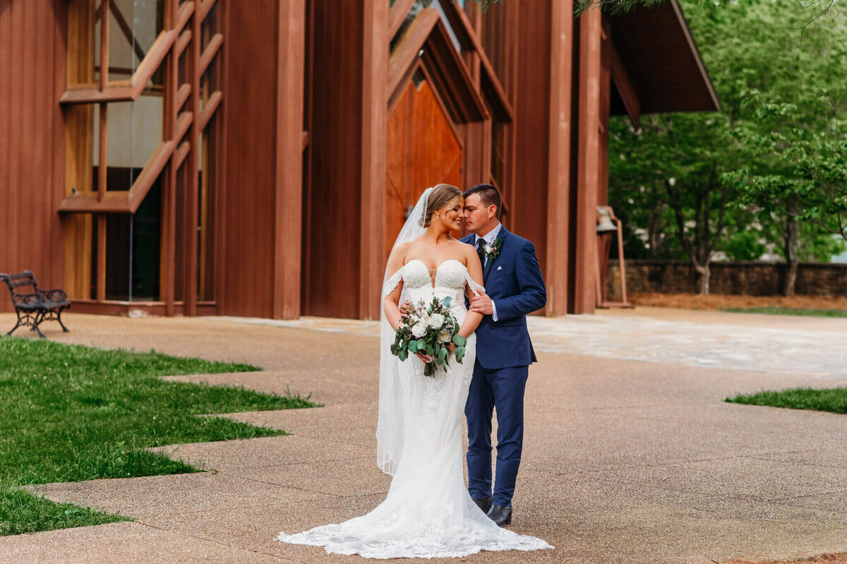 Photo of a groom hugging a bride from behind in front of a wooden wedding chapel