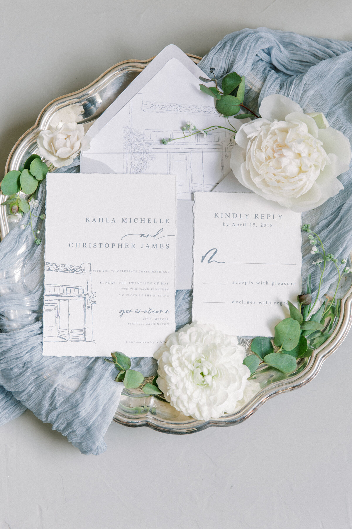 wedding invitation suite with blue cheese cloth and white florals behind it