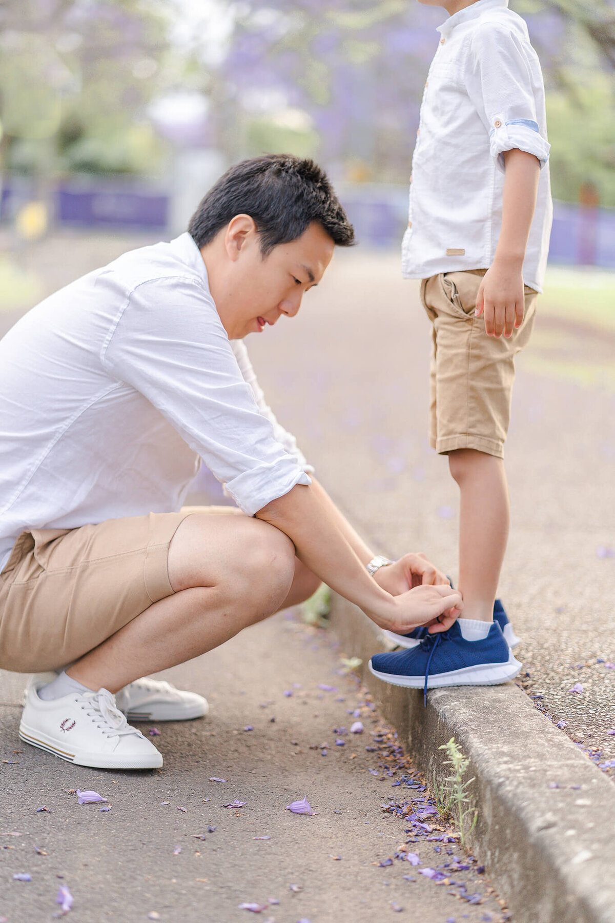 dad helping tie son's shoes in jacaranda blossoms sweet candid moment