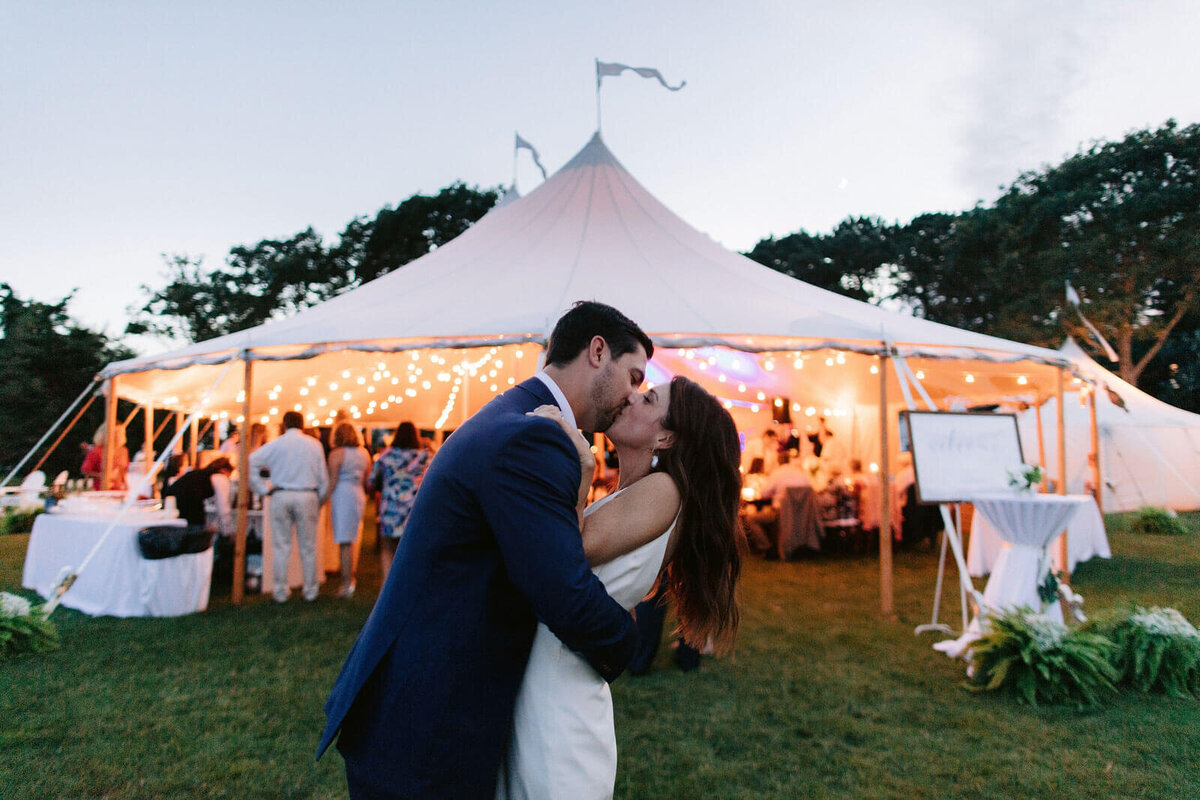 The bride and the groom are kissing in front of Cape Cod Summer Tent, MA.