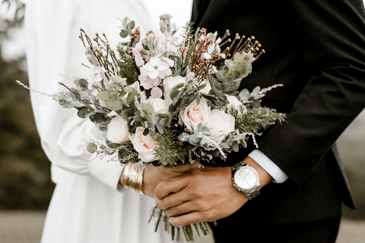 a couple holding a wedding bouquet of flowers together