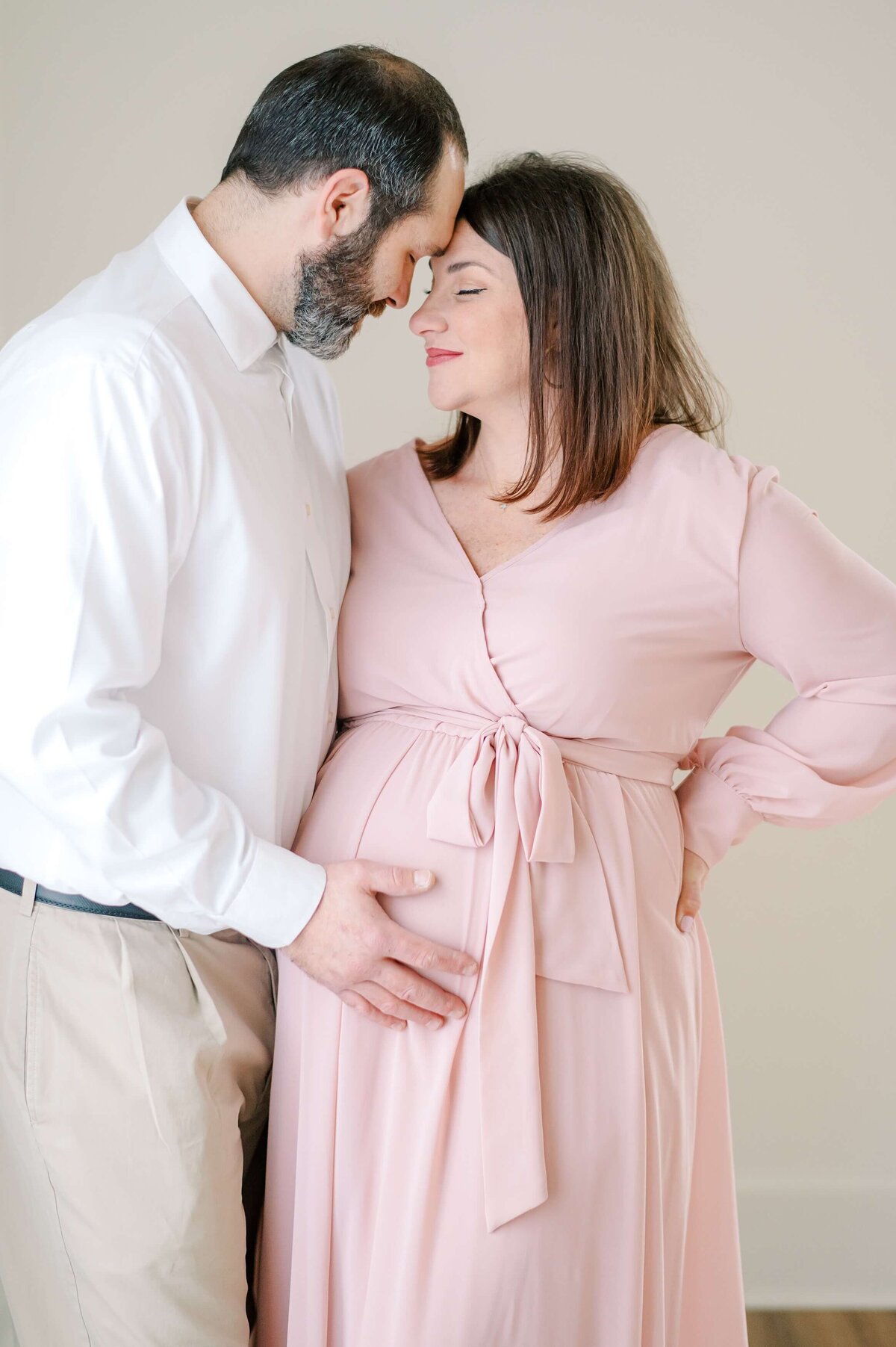 A husband leans his forehead together with his pregnant wife's while lightly touching her baby bump.