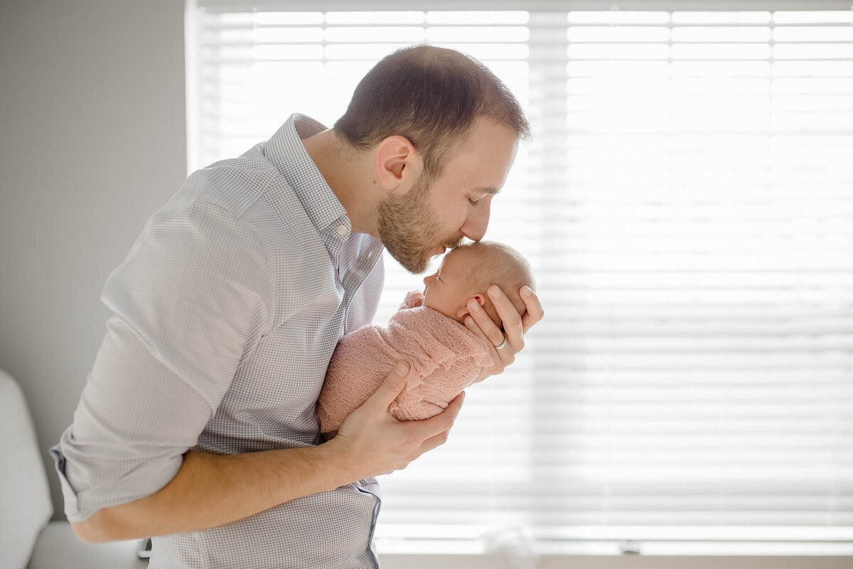 dad kissing baby inside by window