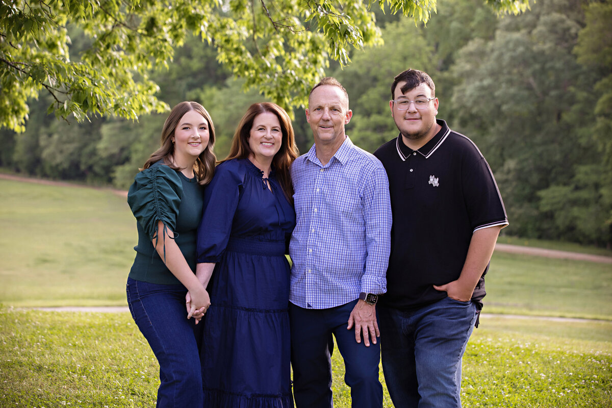 Family of four photographed on a hilltop at Anne Springs Close Greenway by Carolyn Ann Ryan. Mom and Daughter hold hands in front with Dad and son standing close by.